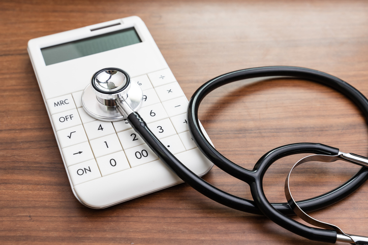 Health care and medical cost expense calculation or financial analysis and saving status concept, doctor stethoscope put on modern white calculator on wooden table
